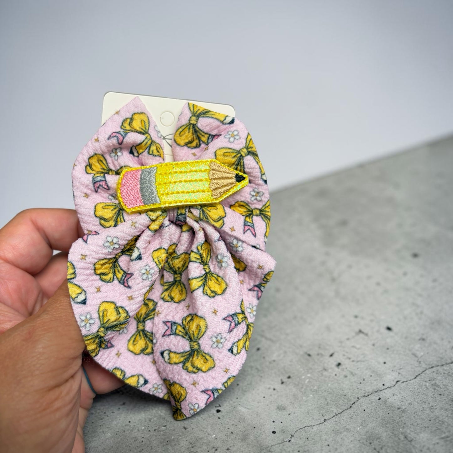 Mloved Designs pastel pink hair bow with yellow pencil appliqué, featuring a whimsical bow and flower pattern.