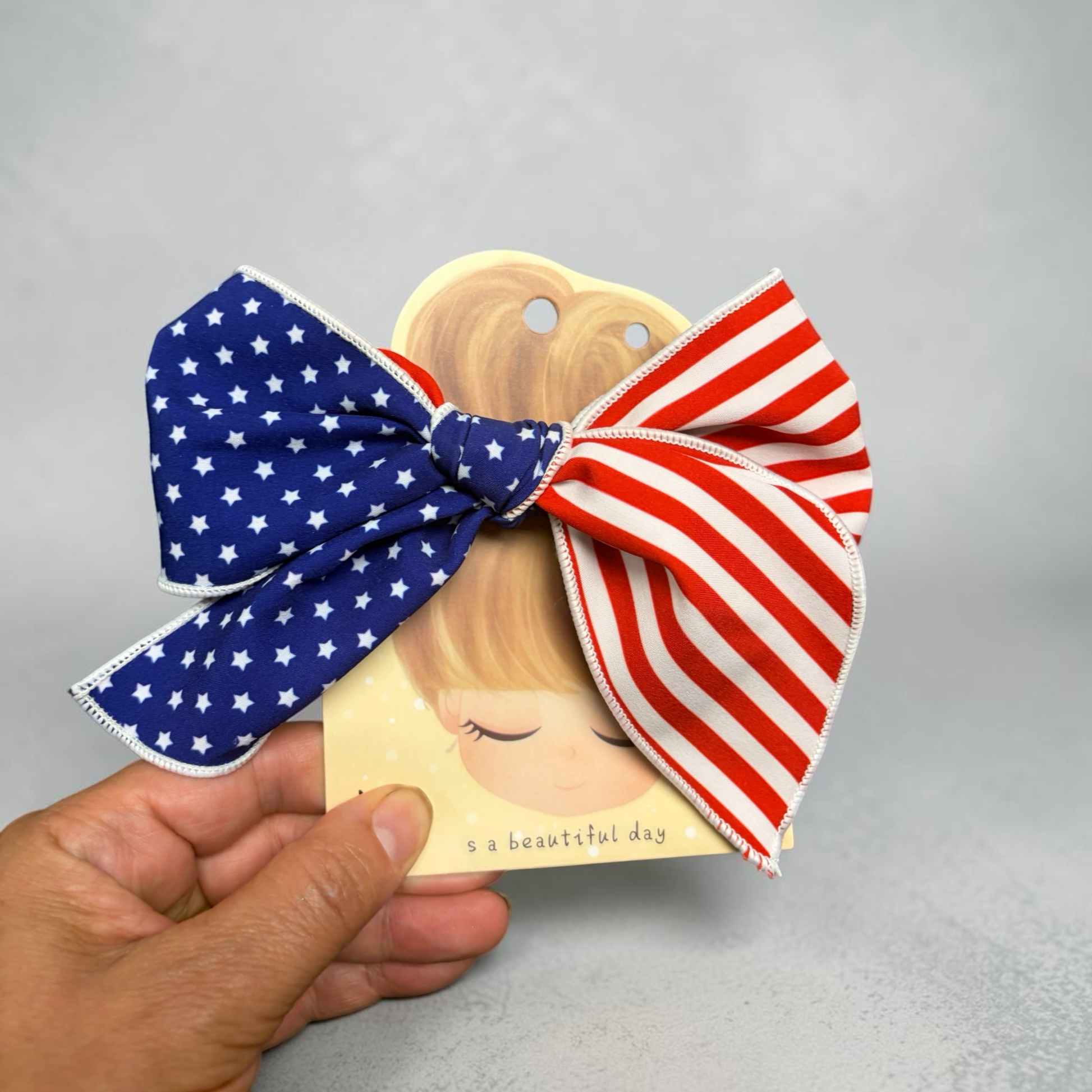 Mloved Designs patriotic hair bow with blue star and red stripe fabric on a decorative display card.
