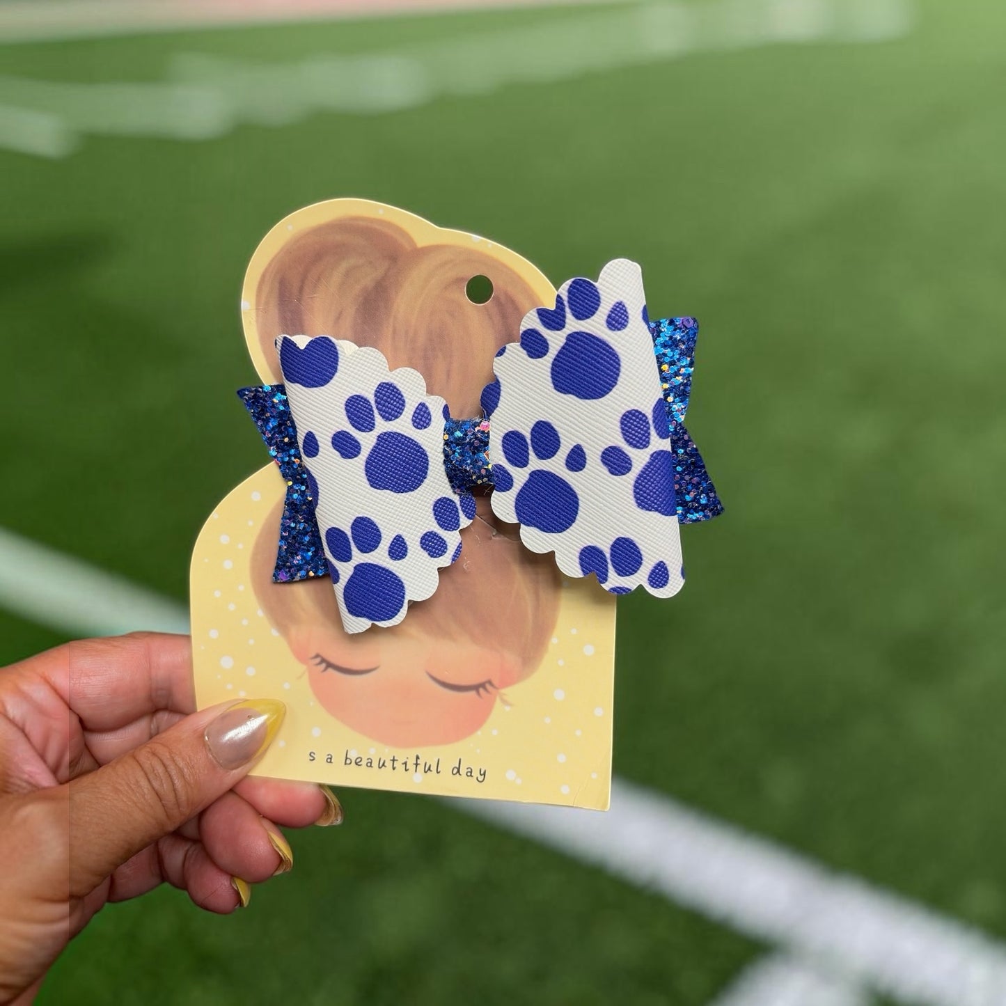 Mloved Designs paw print hair bow with white scalloped edges, blue paw prints, and shimmering blue glitter fabric.